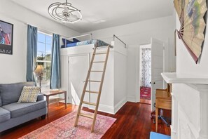 Een kamer met een stapelbed, een ladder, een bank, een klein tafeltje en een kamerkleed met dessin.