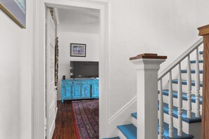 A staircase with white balusters and blue steps leading to a room with a blue cabinet and a flat-screen TV.