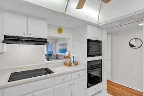 A modern kitchen with white cabinetry, a built-in microwave, a stove, and a ceiling fan. - 7th Heaven by Duncan Real Estate (Longboat Key)