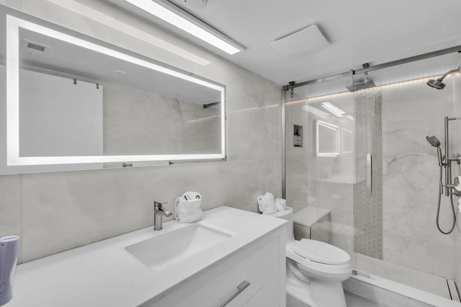 A modern bathroom with a large mirror, a shower, a toilet, and a sink.
