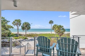 A balcony with two green Adirondack chairs facing a beach with palm trees and a clear blue sky. - 7th Heaven by Duncan Real Estate (Longboat Key)