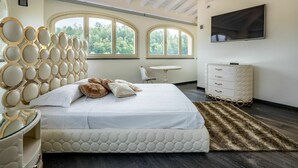 Un dormitorio moderno con una cama grande, un televisor montado en la pared y una ventana con vista a árboles.