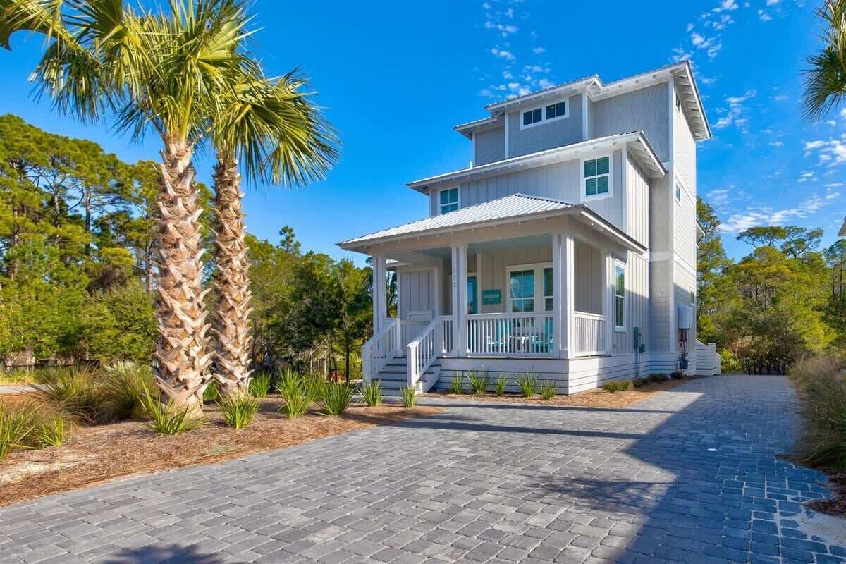 A two-story house with a porch, surrounded by palm trees and a paved driveway.