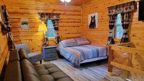 Een gezellig blokhutkamer met een bed, een bankje, een nachtkastje en een houten stoel.