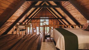 A cozy attic bedroom with a wooden ceiling, a bed with a green throw, a desk with a chair, and a view through a window. - Charming A-Frame @ Mt. Rainier~Nature~Relax! Pet Friendly! (Packwood)