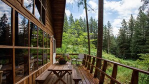 A wooden deck with a table and chairs, overlooking a forested area. - Charming A-Frame @ Mt. Rainier~Nature~Relax! Pet Friendly! (Packwood)