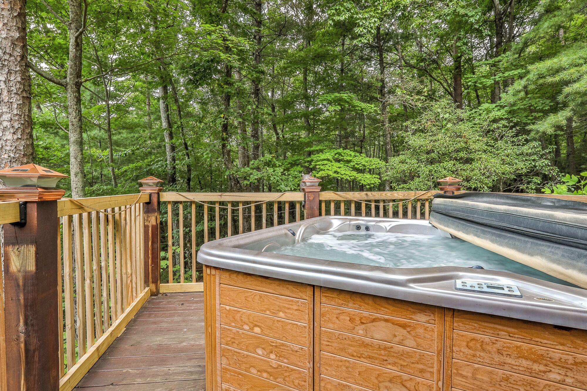 A hot tub on a wooden deck surrounded by a forest.