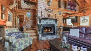 A log cabin interior with a fireplace, leather furniture, and mounted animal heads.