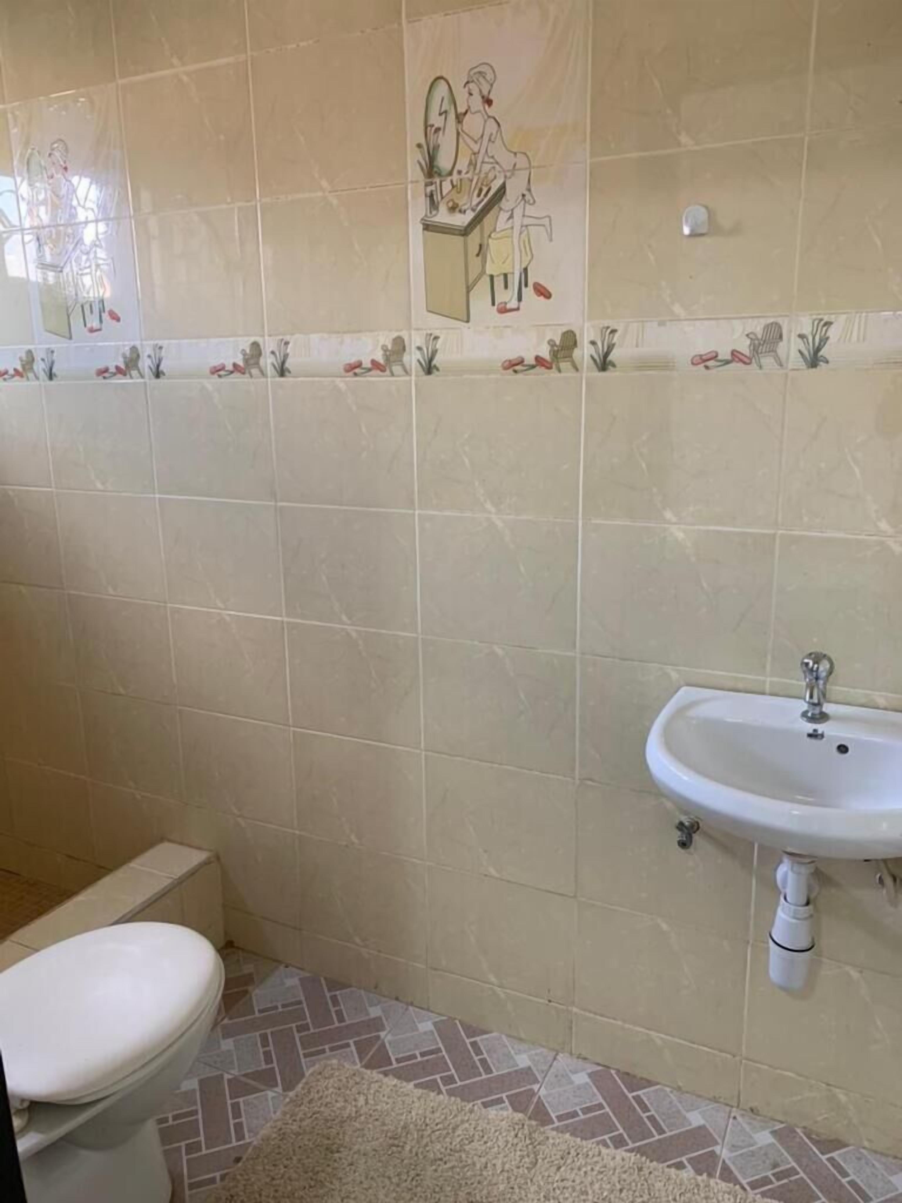 A bathroom with a toilet, a sink, and a decorative tile backsplash.