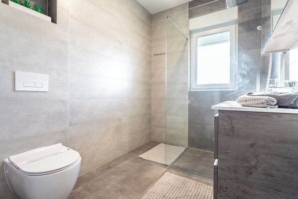 A modern bathroom with a glass shower enclosure, a white toilet, and a wooden vanity with towels.