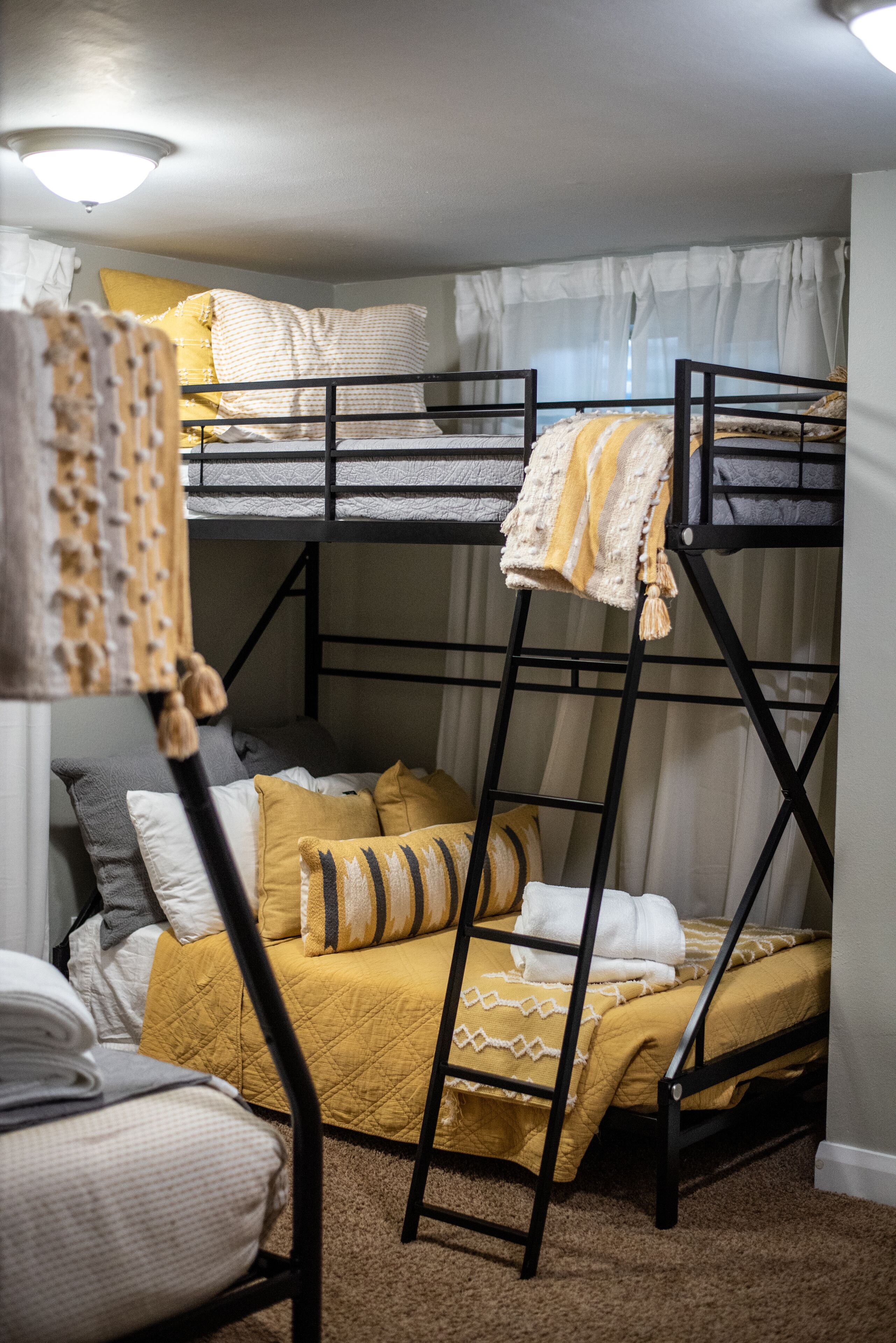 Een slaapkamer met stapelbed, een gele sprei, witte kussens en een zwarte trap.