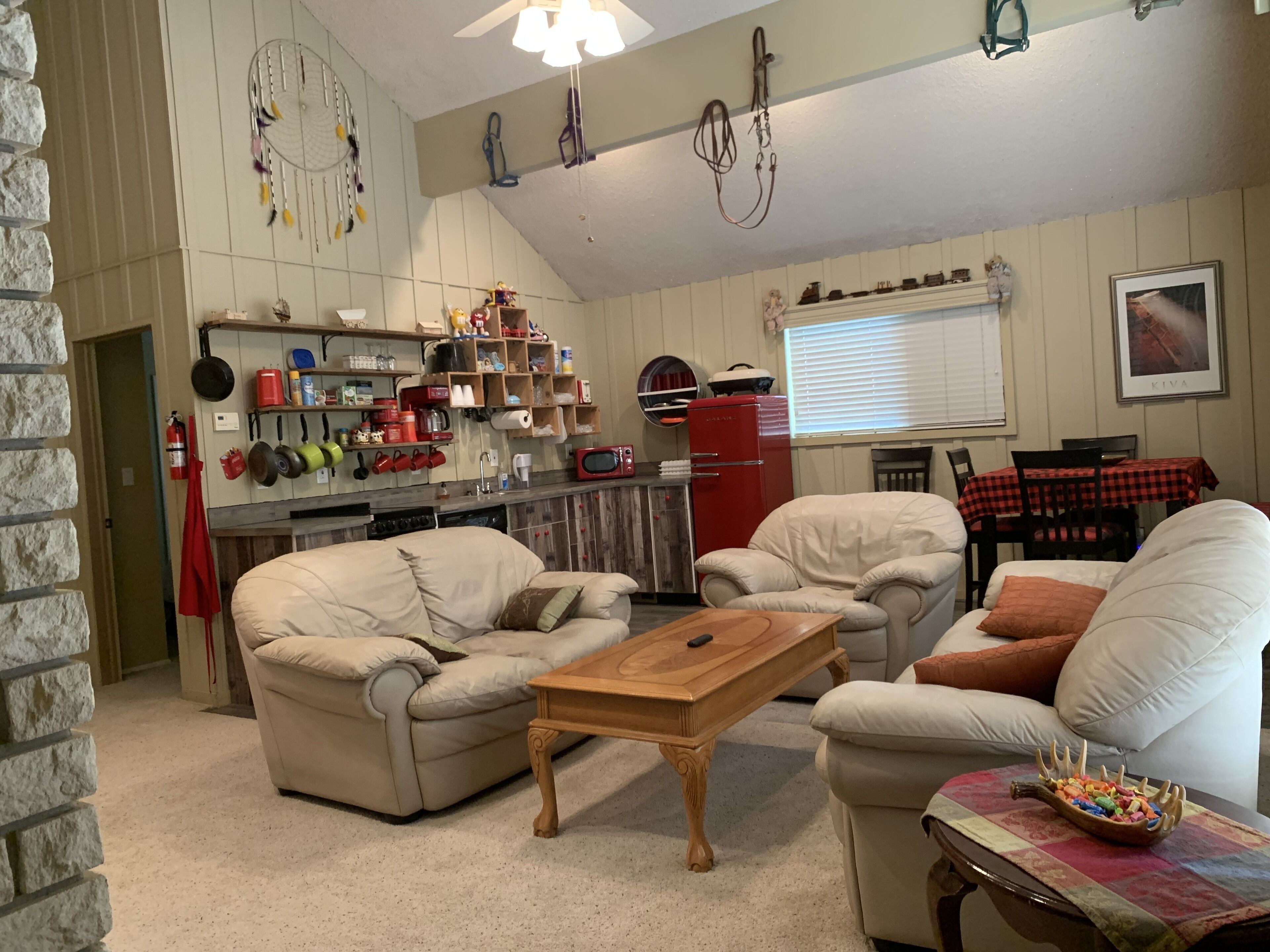 Un salon chaleureux avec une cheminée, un coin repas avec une table et des chaises, et une cuisine équipée de divers appareils et agrémentée de décorations.