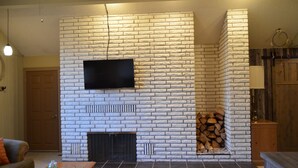 Una sala de estar con chimenea de piedra, un televisor de pantalla plana montado encima y un montón de leña al lado de la chimenea.