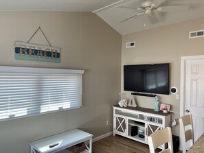 A living room with a TV, a small table, a white cabinet, and a ceiling fan. - Delightful 2-Bedroom Beach Cottage in OBIII (Lavallette)