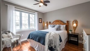 A bedroom with a bed, a chair, a nightstand, and a ceiling fan. - Modern 4BR Lakefront Cottage w/ Hot Tub & Dock (Emsdale)