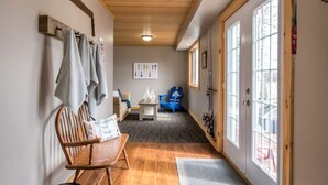 A hallway with wooden flooring, a bench, a chair, and a door with glass panels. - Modern 4BR Lakefront Cottage w/ Hot Tub & Dock (Emsdale)