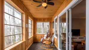 A wooden interior with large windows, a ceiling fan, and a rocking chair. - Modern 4BR Lakefront Cottage w/ Hot Tub & Dock (Emsdale)