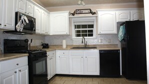 A kitchen with white cabinets, a black stove, a black refrigerator, and a window above the sink.