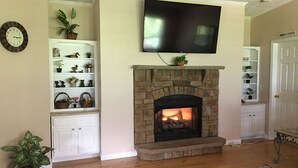 A living room with a stone fireplace, a mounted television, and built-in shelving with decorative items.