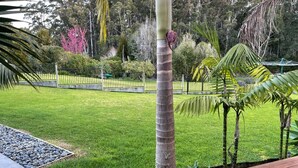 Ein gepflegter Garten mit Rasenfläche, einer Palme und einer Holzterrasse.