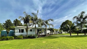 Ein Bungalow mit Veranda, umgeben von einem gepflegten Rasen und Palmen.