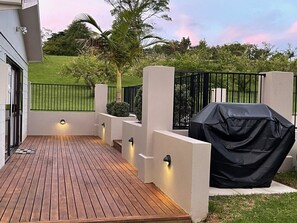 A wooden deck with a barbecue grill, a black fence, and a well-lit outdoor area.