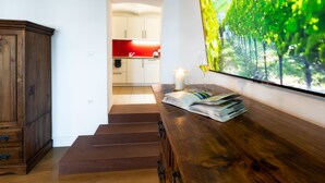 Una cucina moderna con mobili bianchi e una parete di fondo rossa, una scala in legno che conduce a un'altra stanza e un'ampia finestra con vista sugli alberi.