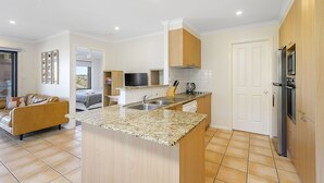 A modern kitchen with granite countertops, wooden cabinets, and stainless steel appliances. - Flynn's Beach Escape ! (Port Macquarie)