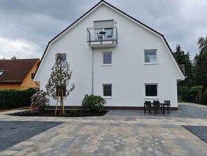 A two-story building with a balcony, a small garden, and a paved patio area.