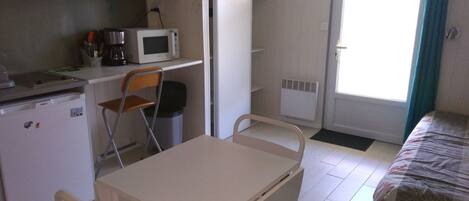 A compact room with a bed, a small kitchenette, a table with a chair, and a television mounted above the counter.