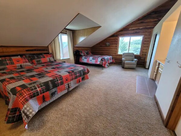 A cozy attic bedroom with two beds, a chair, and a large window.