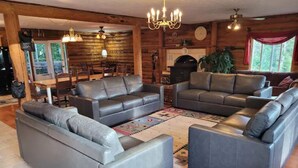 A log cabin interior with two grey sofas, a dining area, and a large window.