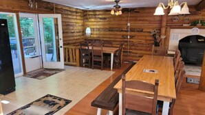 A log cabin interior with a wooden dining table, chairs, a bench, a fireplace, and a grill.