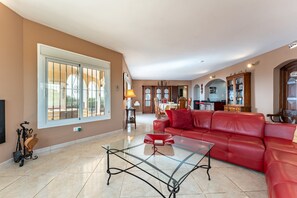 A spacious living room with a red leather sofa, a glass coffee table, and a large window with metal bars.