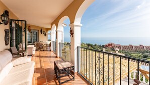 Ein Balkon mit Meerblick, eine weiße Couch, ein kleiner Tisch und ein Geländer.