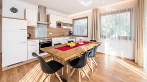 Une cuisine moderne avec des meubles blancs, une table à manger en bois et une grande fenêtre agrémentée de rideaux.