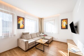 Un salon moderne avec un canapé beige, une table basse en bois et un téléviseur fixé au mur.