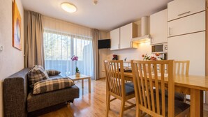 Ein gemütlicher, kompakter Wohnraum mit einer Couch, Esstisch, Stühlen, einer kleinen Küchenzeile mit Mikrowelle und einem Fernseher.
