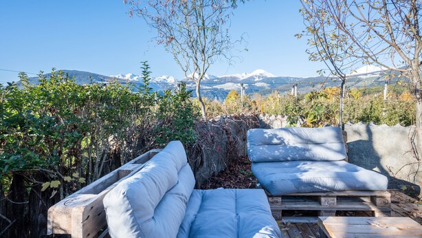 Une terrasse avec deux canapés blancs dotés de coussins, une table en bois et une vue sur des montagnes enneigées.
