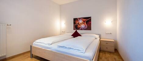 A bedroom with a wooden bed, a red pillow, a nightstand, and a wall-mounted light fixture.