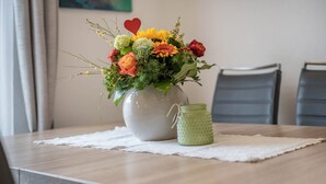 Una mesa de comedor con un jarrón de flores y un pequeño recipiente verde.