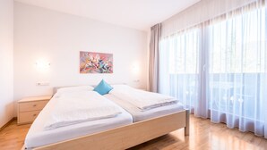 Une chambre moderne avec un lit en bois, une table de chevet, un tableau et des rideaux en voile.