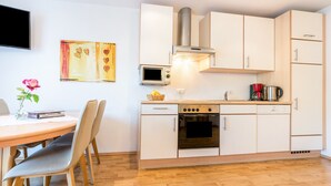 Une cuisine moderne avec des armoires blanches, un four à micro-ondes encastré et une cuisinière. On y trouve une table à manger avec des chaises et un vase avec une fleur.