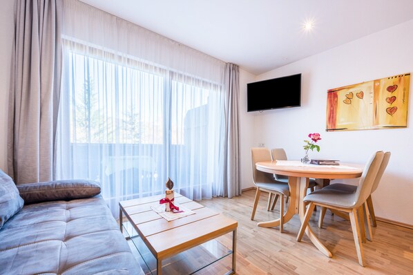 Un salon moderne comprenant un canapé, une table basse en bois, une table à manger avec des chaises, un téléviseur à écran plat et un tableau accroché au mur.