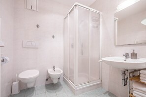 Une salle de bain comprenant des toilettes, un bidet, une douche, un lavabo et un miroir.