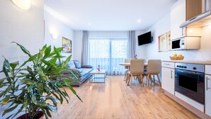 Un salon moderne comprenant un canapé, une table à manger, des chaises, une plante en pot, un téléviseur à écran plat et un coin cuisine avec un four à micro-ondes et un four traditionnel.