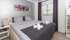 A modern hotel room with a large bed, a bedside table with books, a window with curtains, and a wall art piece. - Apartment "Villa Mar del Plata" with Shared Pool, Wi-Fi, Garden & Terrace (Fuengirola)