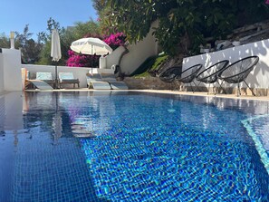 Una piscina con agua azul cristalina, sillas de descanso y sombrillas.