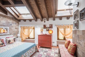 Una camera da letto con un letto, una cassettiera, una panca, una lampada a parete e una finestra con tende.
