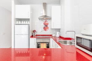 Une cuisine moderne avec des meubles blancs, une hotte en acier inoxydable, un plan de travail rouge, un évier et un four à micro-ondes.